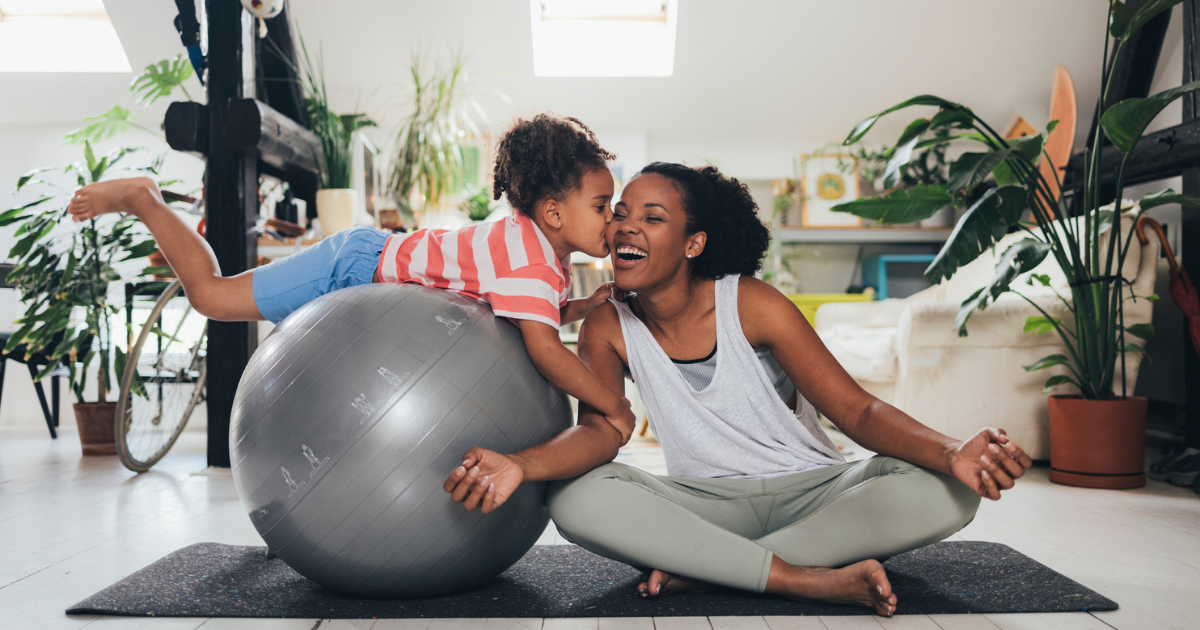 Mom sitting on yoga mat with daughter on exercise ball