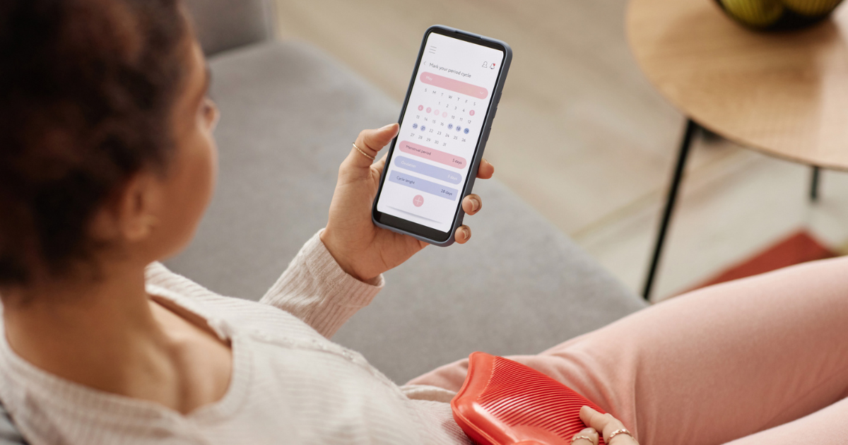 Woman with heating pad looking at calendar app on her phone