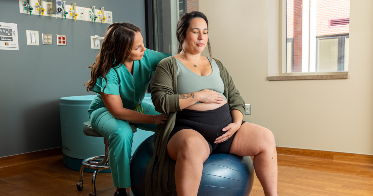 Pregnant woman on exercise ball with midwife kneeling beside her