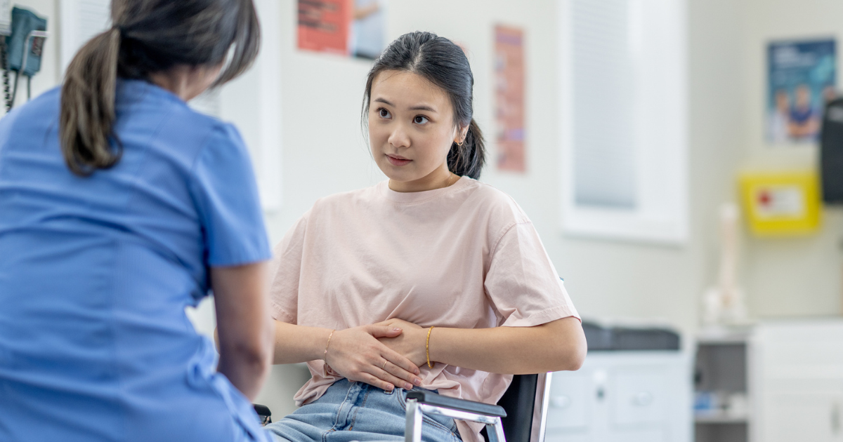 Woman talking to doctor, holding stomach in pain