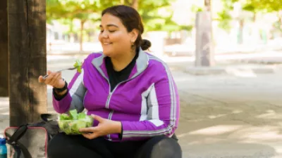 Woman sitting on the sidewalk and eating a salad