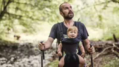 Man wearing a baby in a carrier, hiking in the woods