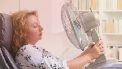 Woman sitting in an office chair and holding a desk fan to her face