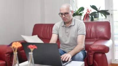 Male cancer patient sitting on couch looking at laptop
