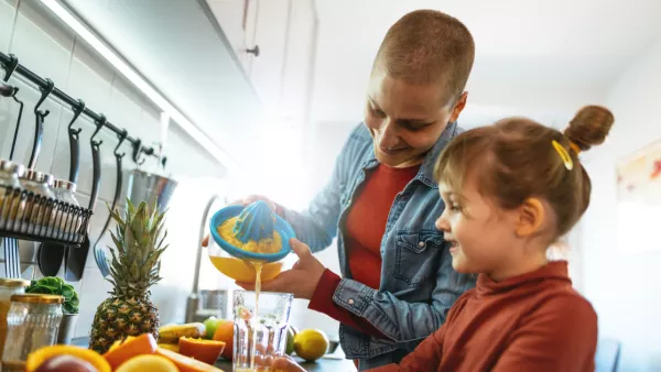 Woman with cancer juicing fruit with young daughter