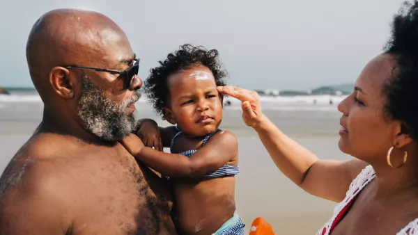 Man holding young girl on beach. Woman applying sunscreen to girl's face