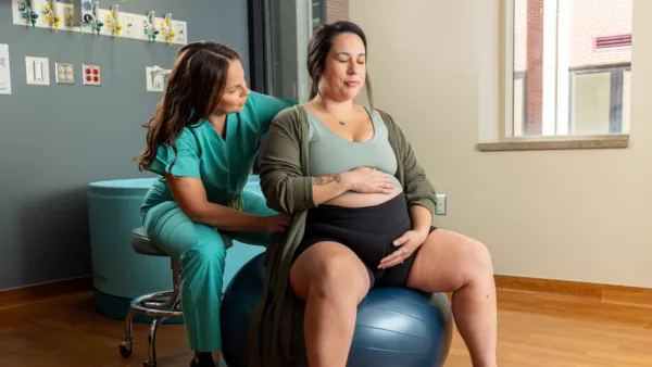 Pregnant woman on exercise ball with midwife kneeling beside her