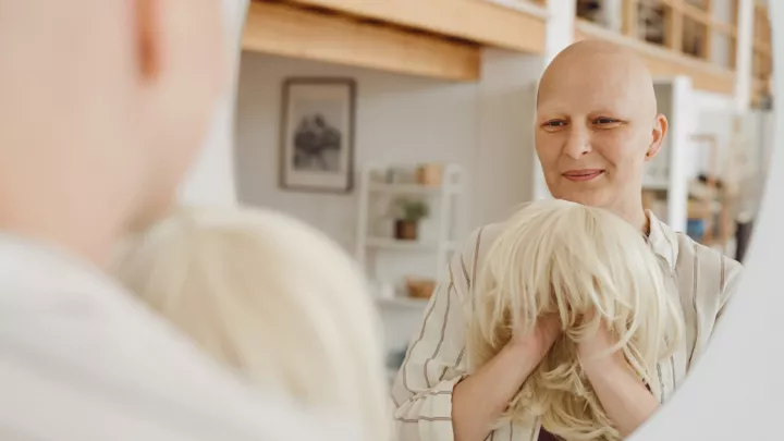 Bald woman holding a blonde wig in front of a mirror