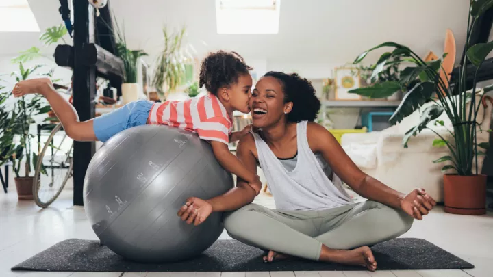 Mom sitting on yoga mat with daughter on exercise ball
