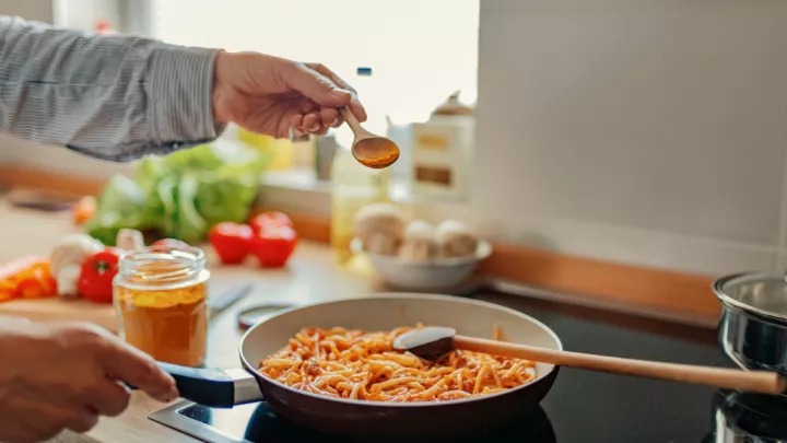 Hand sprinkling turmeric on pasta