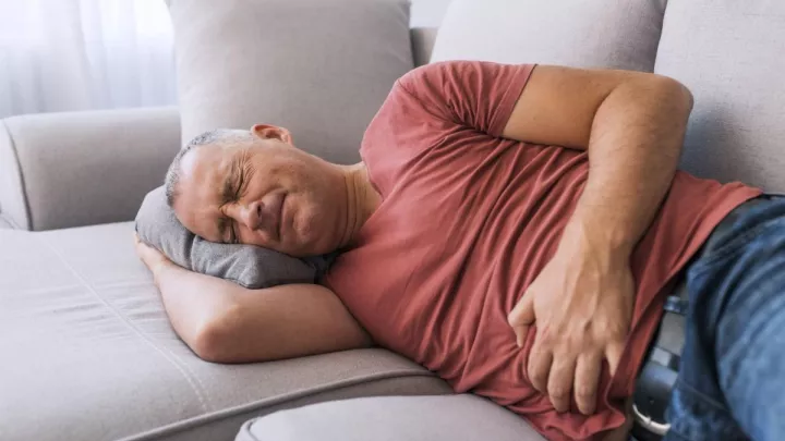 Man laying on couch holding stomach