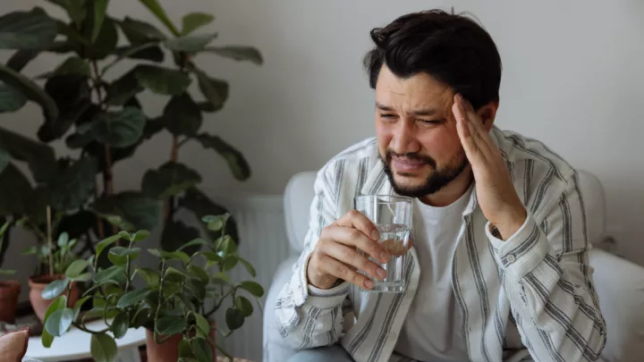 Man holding his head in pain holding a glass of water