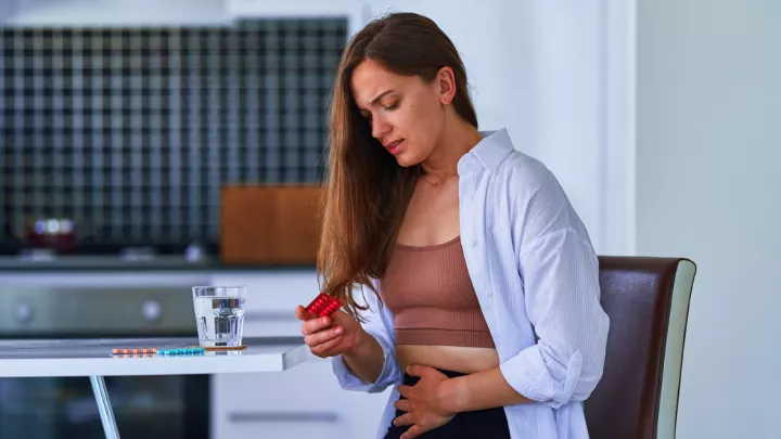 Woman grabbing her abdomen in pain, holding pills
